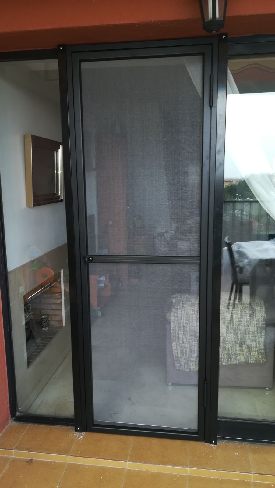 Mosquiteras negras con soporte negro protegiendo sala de estar y puerta.