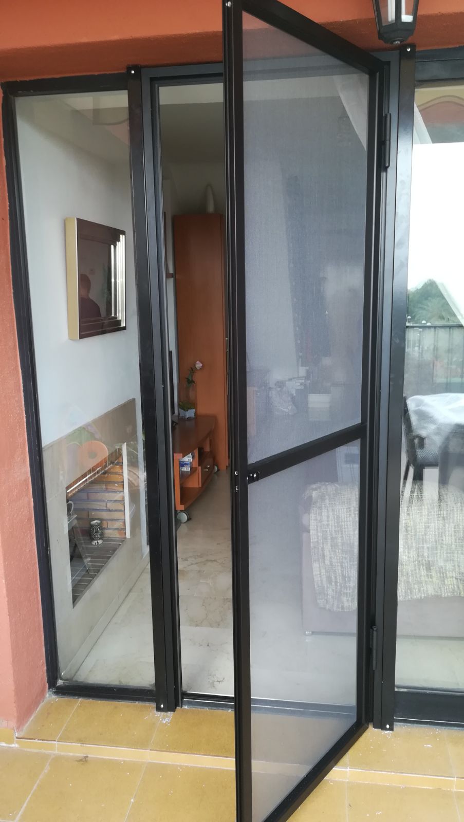Mosquiteras negras con soporte negro protegiendo sala de estar y puerta.