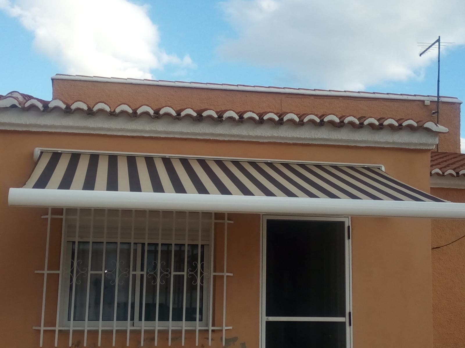 Toldo tipo cofre con brazos extensibles de color negro con blanco.