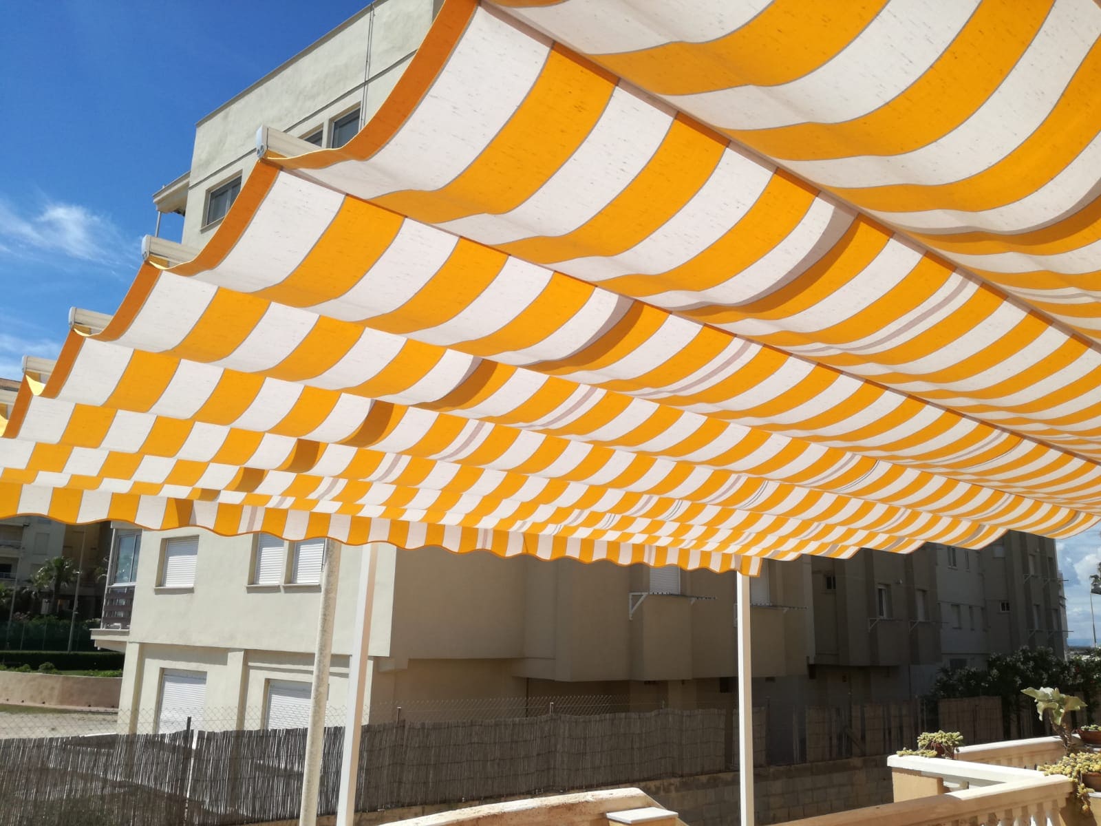 Toldo patio tipo andaluz entre paredes de color amarillo con lineas blancas con motorización