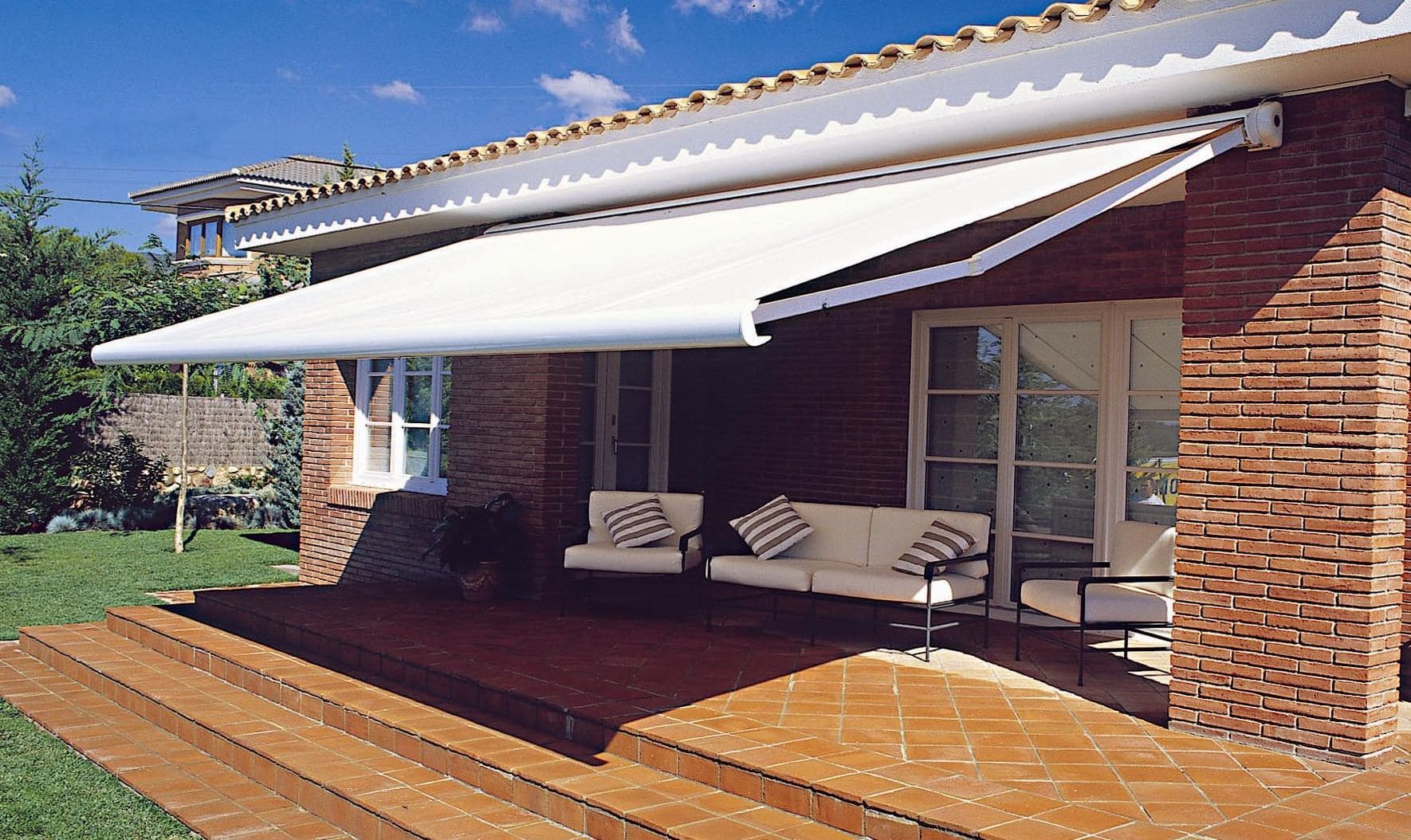 Toldo tipo cofre con brazos extensibles de color blanco en patio de casa.