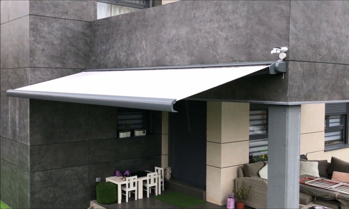Toldo tipo cofre con brazos extensibles de color blanco en patio de casa.